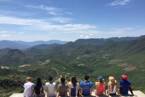 group of students sitting down on ledge and looking over sunny mountain range