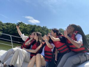 Five students wearing life jackets on a boat pose for a group selfie.