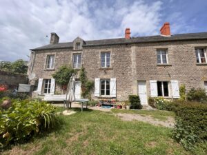 Two story gray stone home with garden and patio furniture in front.