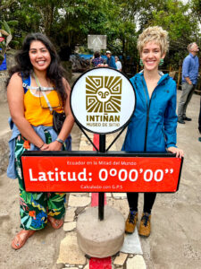 Two female students stand next to a red marker denoting the latitude line as zero degrees.