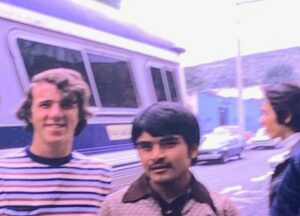 A vintage photo of two young men standing in front of a bus.