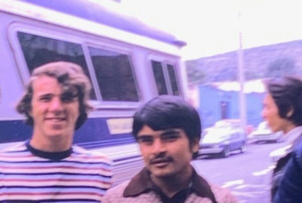 A vintage photo of two young men standing in front of a bus.