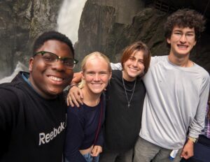Four Experiment in International Living students stand in front of a waterfall with their arms linked around each other's shoulders.