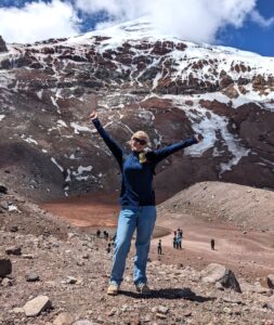An Experiment in International Living student stands with her arms raised on a mountainside. Behind her are snowcapped mountain peaks.