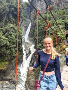 An Experiment in International Living student stands on a suspension bridge. A waterfall running through rocks and trees is behind her.