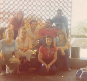 Eight students from The Experiment program are sitting in two rows. They are wearing clothing from the 1970s, and the photo looks older and blurry.