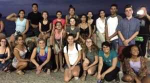 A group of 15 The Experiment high school students pose for a photo. The sky is dark.
