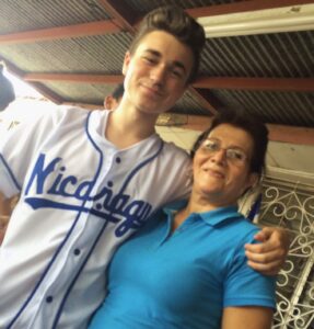 A high school student has his arm around the shoulder of an older woman. He is wearing a Nicaragua baseball jersey.